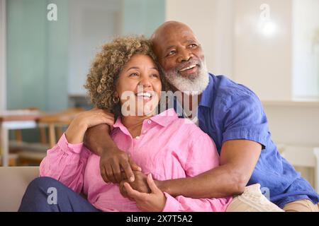 Coppia matura amorevole a casa che abbraccia seduti sul divano nel salotto insieme Foto Stock