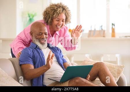 Coppia matura a casa con notebook che effettua videochiamate con la famiglia Foto Stock