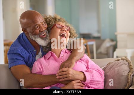 Coppia matura amorevole a casa che abbraccia seduti sul divano nel salotto insieme Foto Stock