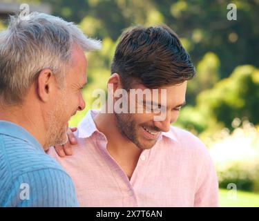 Ridendo e sorridendo il padre maturo che parla con il figlio adulto in piedi all'aperto in campagna Foto Stock