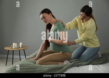 Doula massaggiava una donna incinta in camera da letto. Preparazione alla nascita del bambino Foto Stock