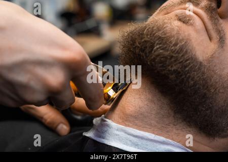 Barber taglia rapidamente la barba dei clienti con un rifinitore automatico nel barbiere Foto Stock