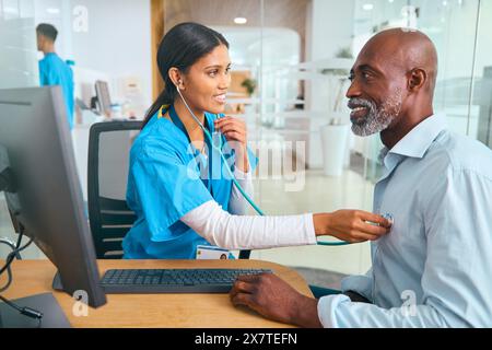 Infermiera o medico che indossa scrub che esamina l'uomo maturo utilizzando lo stetoscopio Foto Stock