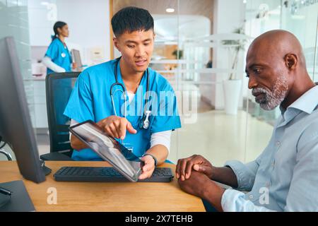 Maschio Dottore in Scrubs all'appuntamento ospedaliero con paziente maschio maturo che guarda Digital tablet Foto Stock