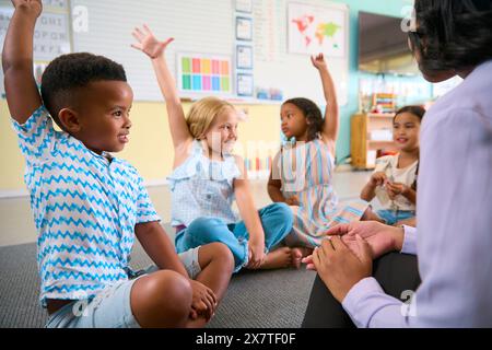 Classe di studenti delle scuole primarie o elementari alzando la mano per rispondere alla domanda in aula Foto Stock