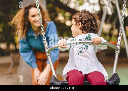 Madre e figlia giocano sullo swing, godendo di un momento di gioia in famiglia, sorridendo e divertendosi, all'aperto, felicità e legame in modo naturale Foto Stock