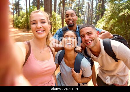 Foto POV di una giovane coppia con amici che posa per Selfie Hiking lungo il sentiero in campagna Foto Stock