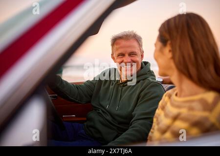 Coppia senior in pensione in vacanza seduto in auto sportiva d'epoca a Beach Watching Sunrise Foto Stock