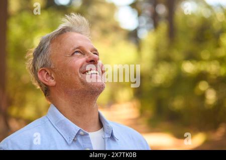 Tranquillo uomo anziano rilassante in mezzo alla natura nella foresta circondata da alberi Foto Stock