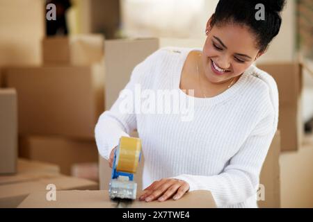 Cassetta per nastro, donna e sorriso in casa per il trasporto, l'imballaggio e il confezionamento per donazioni o beneficenza. Donna, cartone e felice per la vendita a casa con Foto Stock