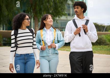 Tre giovani studenti che camminano lungo un marciapiede fuori dall'università Foto Stock