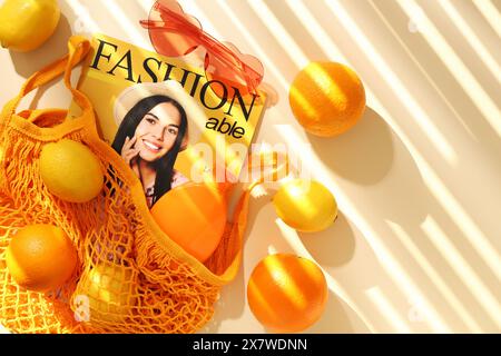 Borsa a cordoncino con frutta fresca, rivista di moda e accessori da spiaggia su sfondo beige, piatto. Spazio per il testo Foto Stock