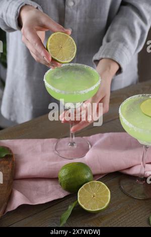 Donna che spreme il succo di lime nel bicchiere con un delizioso cocktail Margarita al tavolo di legno, primo piano Foto Stock