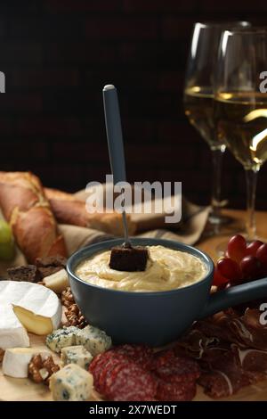 Fonduta con gustoso formaggio fuso, forchetta, diversi spuntini e vino in tavola Foto Stock