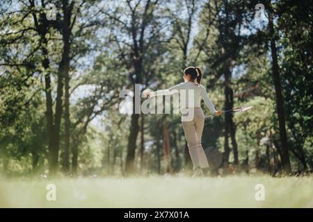 Giovane donna che si gode un momento di pace in una foresta illuminata dal sole, le braccia si spalancano, sentendosi libera e felice Foto Stock