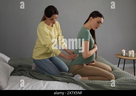 Doula massaggiava una donna incinta in camera da letto. Preparazione alla nascita del bambino Foto Stock