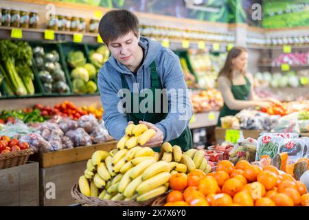 Un giovane venditore che mette le banane in un cestino del mercato in un grande negozio di alimentari Foto Stock