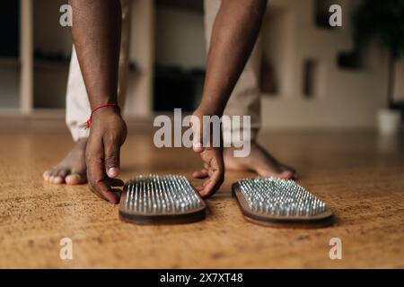 Primo piano ritagliato di un irriconoscibile maschio nero a piedi nudi che si prepara a salire sulla tavola Sadhu in legno con unghie di metallo durante le esercitazioni a casa. Foto Stock