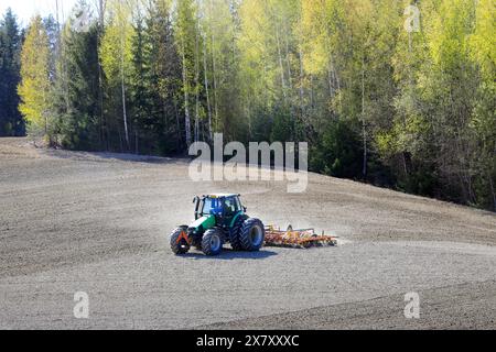 Coltivare campi con trattore Deutz-Fahr Agrotron e erpice Tume in primavera. Paesaggio agricolo con spazio di copia. Salo, Finlandia. 10 maggio 2024. Foto Stock