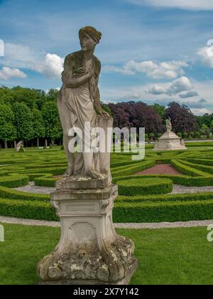 Statua in pietra di una donna in un giardino barocco ben tenuto con siepi simmetriche e cielo nuvoloso, parco con siepi verdi, piccoli sentieri e vecchie statue, Nor Foto Stock
