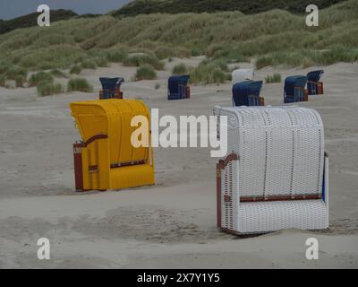 Una sedia da spiaggia gialla e una bianca sono in piedi sulla spiaggia, con dune e molti altri cesti sullo sfondo, sedie da spiaggia colorate sul beac Foto Stock