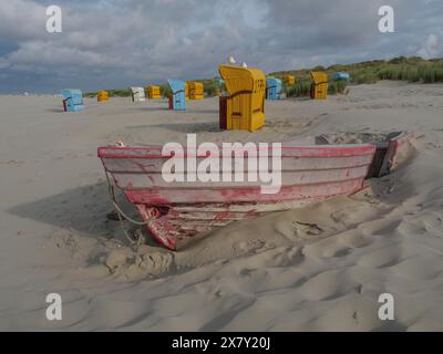 Una vecchia barca è sepolta nella sabbia, circondata da sedie da spiaggia colorate e cielo nuvoloso, sedie da spiaggia colorate sulla spiaggia e tra le dune con clou Foto Stock