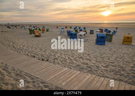 Una spiaggia tranquilla al tramonto con sdraio colorate, una passerella in legno e sabbia soffice, molte sdraio colorate in una calda serata estiva Foto Stock