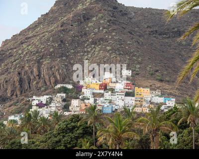 Piccolo villaggio con case colorate su una montagna rocciosa, circondato da palme e vegetazione lussureggiante, montagne e valli su un'isola nell'Atlan Foto Stock