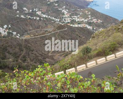 La strada tortuosa conduce attraverso un paesaggio montuoso giù verso le case costiere con vista sul mare, montagne e valli su un'isola nell'atlantico con Foto Stock