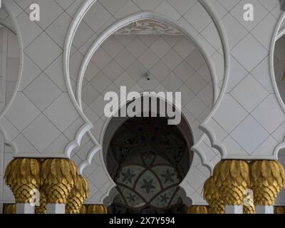 Vista interna con archi e ornamenti dorati su pareti bianche, moschea bianca con torri e cupole e colonne dorate, Abu Dhabi, Emirati Arabi Foto Stock