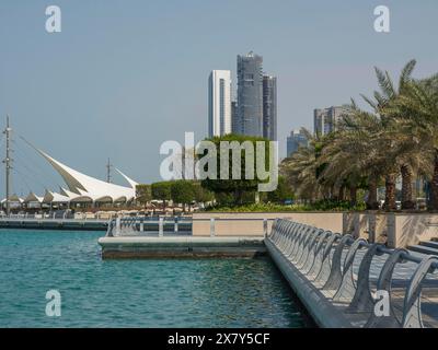 Edifici moderni e palme verdi lungo una tranquilla passeggiata costiera con il bel tempo, passeggiata costeggiata da palme sul mare con grattacieli e lanterne, Foto Stock