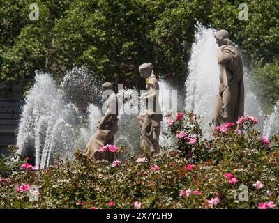 Tre statue in una fontana circondata da fiori fioriti e fontane gorgoglianti, fontana con figure di fronte a un edificio storico, barcel Foto Stock