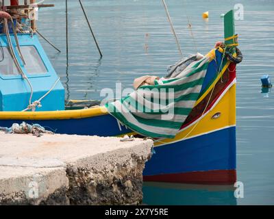 Piccola barca colorata ormeggiata al molo, coperta da un panno a righe, molte barche da pesca colorate in un porto nel Mar Mediterraneo, Marsaxlokk, Foto Stock