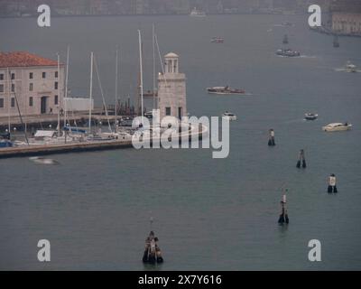 Porto di Venezia con numerose barche e yacht e un muro di cinta in un'atmosfera nebbiosa, torri di chiese ed edifici storici su un grande canale, vista su Foto Stock