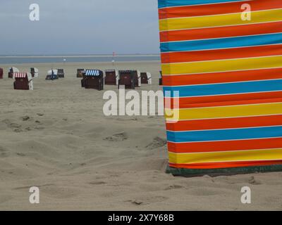 Una colorata striscia di sabbia sulla spiaggia con sedie a sdraio sullo sfondo, ampia sabbia, sedie a sdraio e tende da spiaggia sul mare sotto un cielo nuvoloso Foto Stock