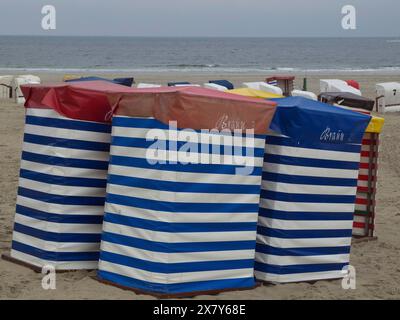 Diverse sedie da spiaggia colorate con motivi a strisce in piedi sulla spiaggia di fronte a un cielo nuvoloso, sedie da spiaggia e tende da spiaggia in riva al mare sotto un clo Foto Stock