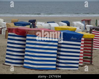 Fila di sedie da spiaggia colorate con motivi a strisce sulla spiaggia con vista sul mare, sedie da spiaggia e tende da spiaggia sul mare sotto un cielo nuvoloso, boa Foto Stock