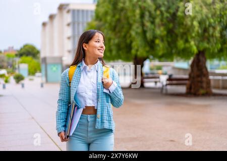 Felice studente universitario asiatico che cammina lungo il suo campus sorridendo e guardando da parte Foto Stock