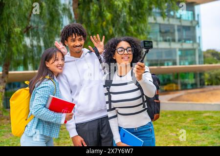 Tre studenti multietnici che salutano mentre registrano un video con una videocamera indossabile in piedi fuori dal campus Foto Stock