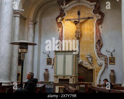 L'interno solenne di una chiesa con un crocifisso sopra l'altare, illuminazione calda e persone che pregano sulle panchine, Catania, italia, 3 febbraio 2024, 3 da Foto Stock