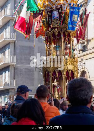 Una folla si riunisce per una celebrazione religiosa intorno a una statua ornata con bandiere, su una strada con edifici antichi, Catania, italia, 3 febbraio 2024, 3D. Foto Stock