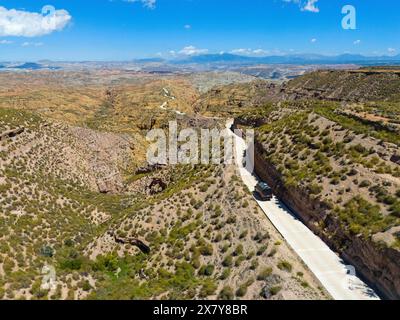 La strada asfaltata si snoda attraverso un vasto paesaggio desertico roccioso con cielo limpido, vista aerea, guida in camper lungo strade strette, deserto di Gorafe, Granada, e. Foto Stock