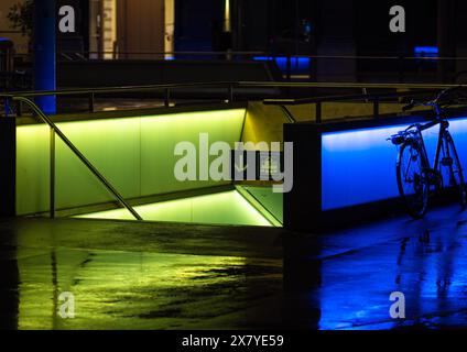 Zurigo, Svizzera - 16 maggio 2024: Vivace scena notturna con ingresso della metropolitana illuminato da luce giallo-verde, terreno bagnato che riflette colori vivaci, urbano Foto Stock