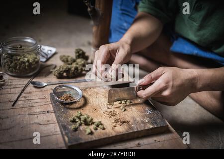 Un uomo prepara marijuana su un tagliere per fumare, persona che fuma droga, tossicodipendenza, tossicodipendenza e sintomi di astinenza. DrugsInte Foto Stock