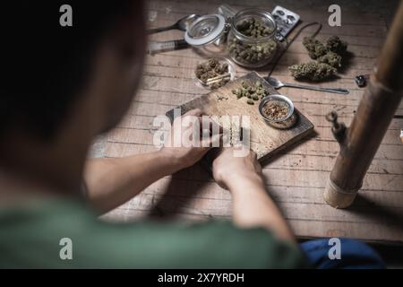 Un uomo prepara marijuana su un tagliere per fumare, persona che fuma droga, tossicodipendenza, tossicodipendenza e sintomi di astinenza. DrugsInte Foto Stock