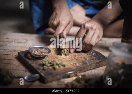 Un uomo prepara marijuana su un tagliere per fumare, persona che fuma droga, tossicodipendenza, tossicodipendenza e sintomi di astinenza. DrugsInte Foto Stock