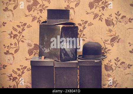Immagine in stile retrò di cappelli da gentiluomo neri vintage con scatole intemperie davanti alla vecchia carta da parati Foto Stock