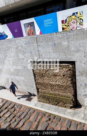 Uomo che cammina lungo la vecchia strada del porto romano vicino alla cattedrale, sopra ci sono le foto su una recinzione di costruzione del Museo Romano-Germanico di Colonia, Ger Foto Stock