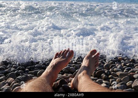 I piedi dell'uomo sulla spiaggia di ciottoli di fronte al mare Foto Stock