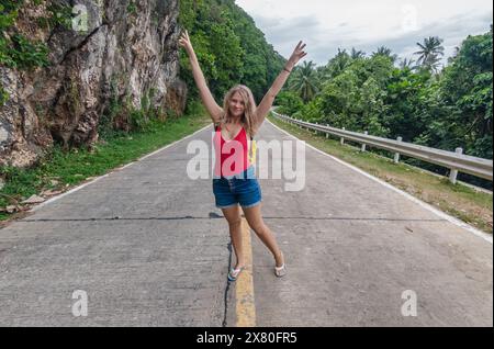 Giovane donna che posa su una strada panoramica di montagna in un ambiente tropicale durante il giorno Foto Stock